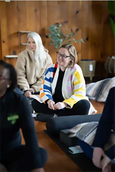A group of people sit comfortably on cushions in a cozy, wood-paneled room, sharing smiles and laughter during a peaceful retreat at South Shore Resort and Retreats, a serene West Michigan vacation rental ideal for relaxation and connection.| South Shore Resort & Retreats in West Michigan
