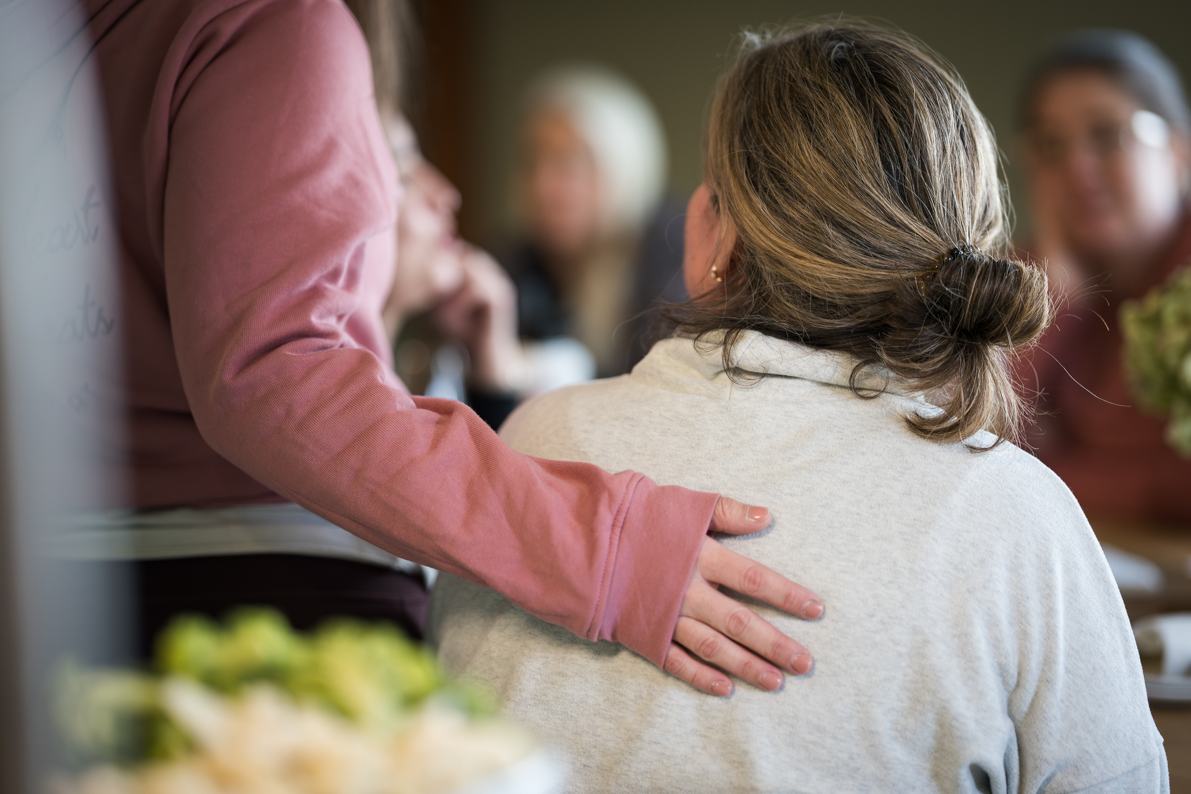 A person in a pink sweater gently rests a hand on another person's shoulder in a comforting gesture, capturing the warmth and connection at South Shore Resort and Retreats, ideal for a peaceful retreat or Lake Michigan getaway.| South Shore Resort & Retreats in West Michigan